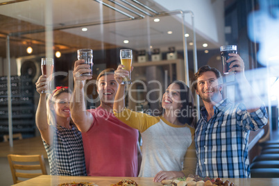 Cheerful friends with hand raised holding beer glass in bar