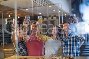 Cheerful friends with hand raised holding beer glass in bar