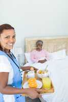 Smiling female doctor serving breakfast to senior woman on bed