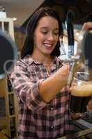 Smiling young barmaid pouring drink from tap in glass