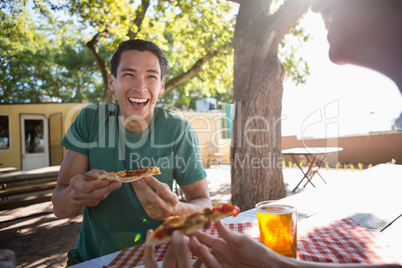Happy man looking at friend while having pizza