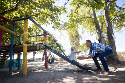 Father looking at son sliding at playground