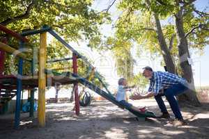 Father looking at son sliding at playground