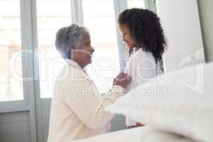 Grandmother dressing up her granddaughter in bedroom