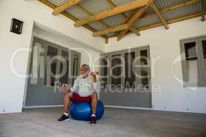 Senior man exercising with dumbbells on exercise ball in the porch