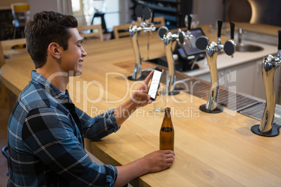 Man with beer bottle using phone at bar