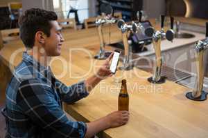 Man with beer bottle using phone at bar