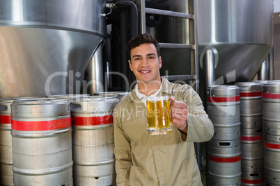 Portrait of smiling man holding beer glass against storage tanks