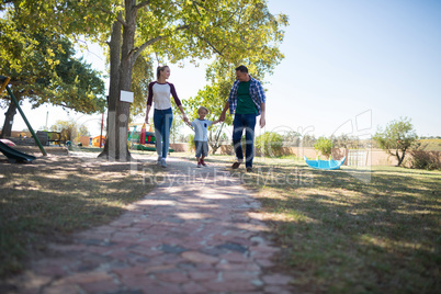 Full length of parents and son holding hands while walking on footpath