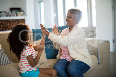 Granddaughter and grandmother playing clapping games on sofa in living room