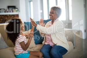Granddaughter and grandmother playing clapping games on sofa in living room