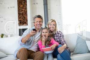 Smiling family watching television while having popcorn in living room