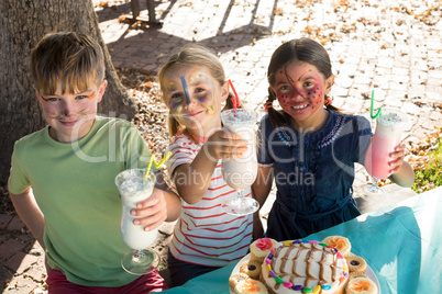 Portrait of children holding drinks while standing at table in park