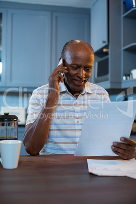 Smiling man reading document while using phone at home