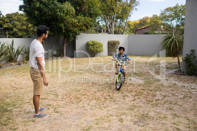 Father looking at son riding bicycle