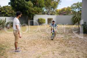 Father looking at son riding bicycle
