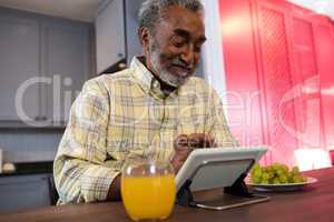 Happy senior man using tablet computer in kitchen