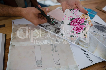Cropped hands of designer cutting papers at table