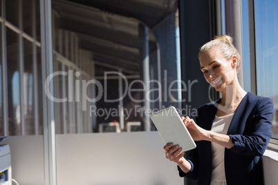 Smiling businesswoman using digital tablet while standing by window