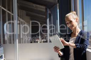 Smiling businesswoman using digital tablet while standing by window