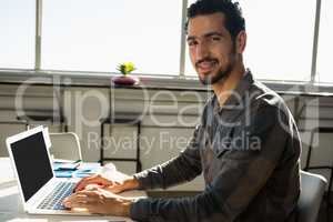 Portrait of man using laptop at desk in office