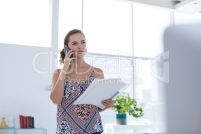 Female executive talking on mobile phone while holding document