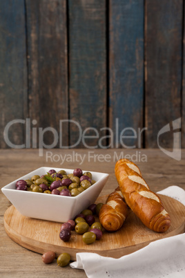 Olives in container by bread on cutting board against wall