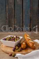 Olives in container by bread on cutting board against wall
