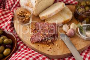 Chili flakes on meat by bread with olives in jar
