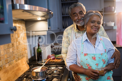 Portrait of couple standing by stove in kitchen