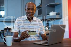 Portrait of man holding credit card while using laptop