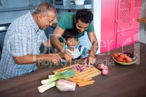 Smiling man looking at boy cutting onion with father