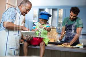 Grandfather showing tablet to grandson while preparing food