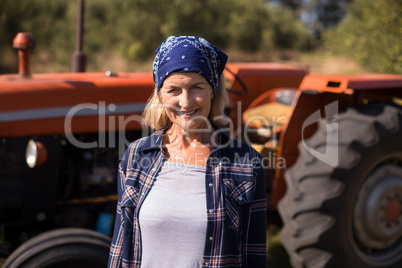 Portrait of happy woman standing against tractor in olive farm