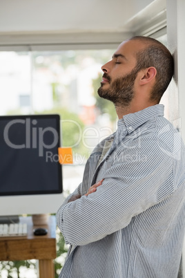 Designer with arms crossed relaxing while leaning on wall