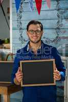 Smiling owner holding writing slate while standing by cafe