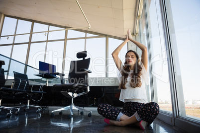 Businesswoman with eyes closed doing yoga on floor