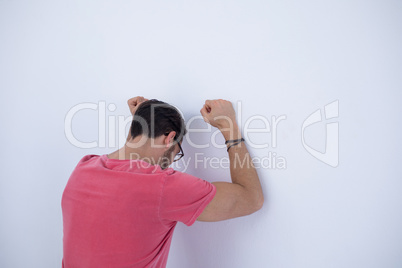 Depressed male executive with arms raised leaning on wall