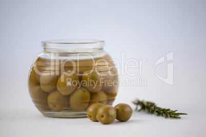 Close of green olives in glass jar by herb