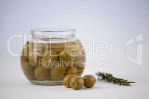 Close of green olives in glass jar by herb