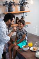 Father feeding cereal breakfast to son sitting on table