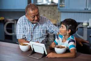 Grandfather and grandson using tablet computer during breakfast