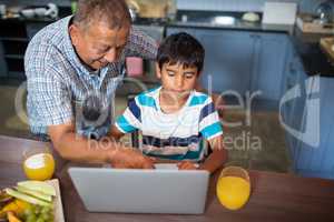 High angle view of smiling grandfather assisting grandson using laptop