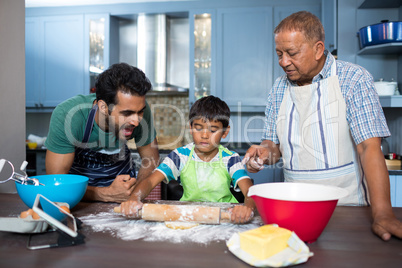 Father shouting with son rolling dough while standing by grandfather