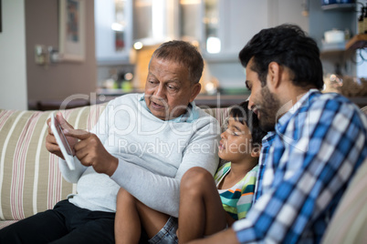 Grandfather showing tablet to grandson sitting with father at home