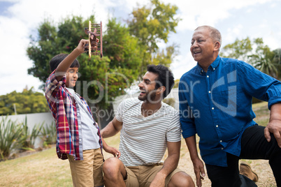 Boy showing toy airplane to father crouching by senior man