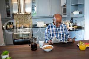 Senior man reading newspaper while having breakfast