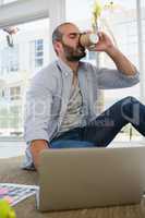 Designer having drink while sitting by laptop on floor