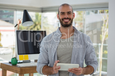 Portrait of smiling designer using digital tablet while standing in office