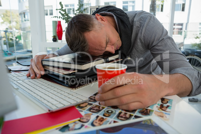 Businessman holding cup sleeping on files at desk